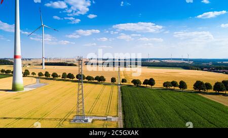 Luftaufnahme der Windmühle gegen blauen Himmel mit Wolken. Windturbinenpark und eine Straße zwischen landwirtschaftlichen Feldern Stockfoto