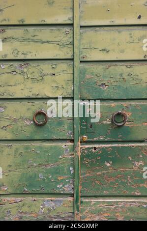 Detail einer alten verfallenen grünen Tür mit rissiger Farbe Hintergrund und verrostete Türgriffe Stockfoto