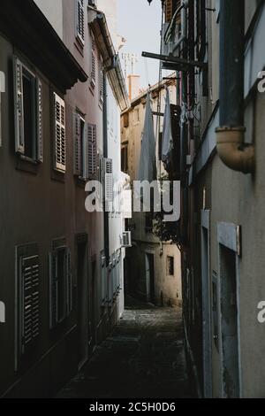 Romantische enge Gasse der alten historischen Küstenstadt Piran in Slowenien von Häusern mit geschlossenen Fensterläden und hängenden Trocknungskleidung gesäumt Stockfoto