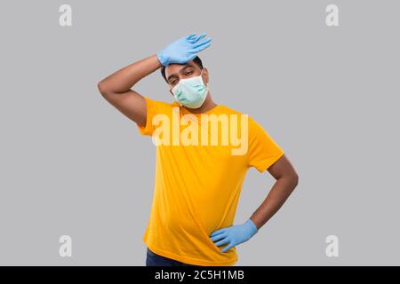 Indian man müde Zeichen tragen medizinische Maske und Handschuhe. Mann, der Schweiß abwischt, isoliert Stockfoto