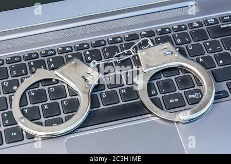 Handschellen, die auf der Computertastatur liegen, als Symbol für Cyberkriminalität Stockfoto