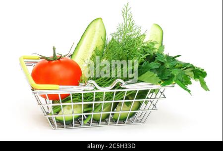 Ein kleiner Einkaufskorb mit Kräutern, Gurke, Tomate, Petersilie neben einem frischen, eingetopften grünen Salat auf weißem Grund. Gesunde Ernährung, vegetarische Kost, Stockfoto