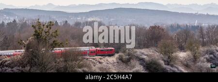 Rote Bahn durch oberbayerische Landschaft. Panorama mit Bäumen und Bergen (alpen) in der Ferne. Stockfoto