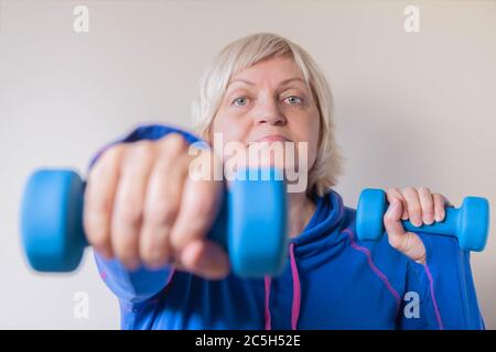 Porträt einer älteren Frau in blau mit Hanteln. Aktive ältere Frau Hanteln heben. Nahaufnahme der älteren Frau bei Übungen mit Hanteln Stockfoto