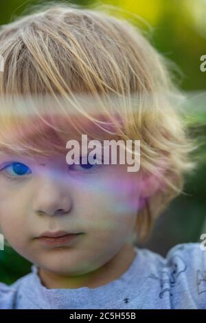 Junge Vorschuljunge weht riesigen Regenbogen Blasen in einem Hinterhof Einstellung Stockfoto