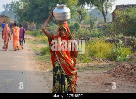 TIKAMGARH, MADHYA PRADESH, INDIEN - 12. NOVEMBER 2019: Eine nicht identifizierte indische Dorffrau trägt Wasser auf ihren Köpfen in traditionellen Töpfen aus Brunnen. Stockfoto