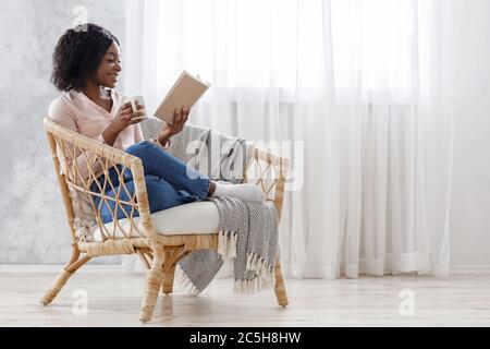 Freizeit Zu Hause. Happy black girl Buch lesen und Kaffee trinken im Sessel Stockfoto