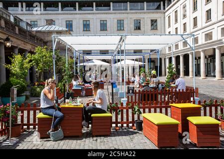 Die Leute sitzen in Covent Garden piazza beim Mittagessen in gesellschaftlich entfernten Sitzbereichen, London, Großbritannien Stockfoto