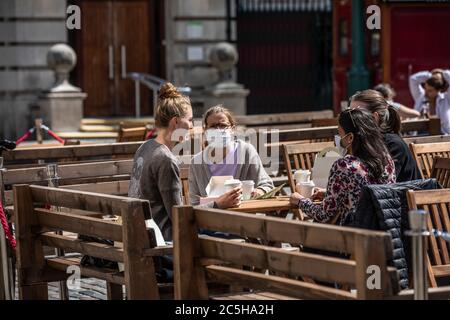 Eine Gruppe von Freunden sitzt in Covent Garden piazza beim Mittagessen in gesellschaftlich entfernten Sitzbereichen, London, Großbritannien Stockfoto