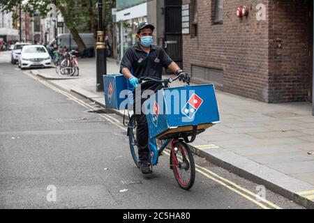Domino's Pizza Lieferfahrradfahrer trägt Schutzmaske und Handschuhe während seiner Runde in Zentral-London, England, Großbritannien Stockfoto