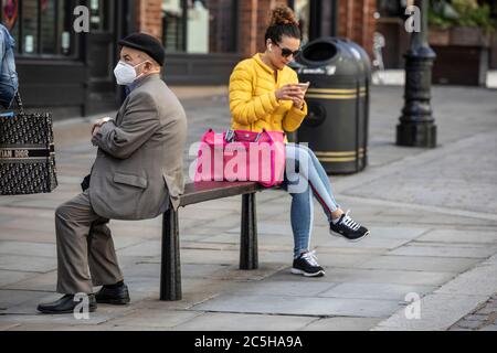 Der Rentner sitzt auf einer Straßenbank, hält sich an die soziale Distanz des Coronavirus, während er eine Gesichtsmask in Covent Garden, West End London, trägt Stockfoto