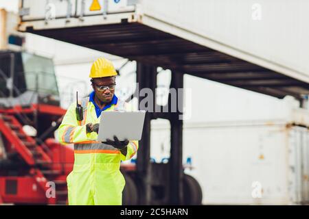 Schwarz afrikanischen Arbeiter in der logistischen Schifffahrt mit Laptop, um die Verladung Container im Hafen Fracht für Import Exportwaren Vorarbeiter suchen hig zu steuern Stockfoto