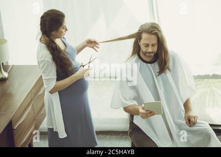 Schwangere Frau bekommt einen Haarschnitt für den Mann, während zu Hause bleiben, wie schön warm und liebevolle Familie Moment vintage Farbe Ton. Stockfoto