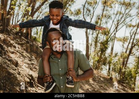 Mann, der seinen Sohn auf den Schultern trägt, während er auf einem Bergpfad geht. Vater und Sohn haben eine tolle Zeit zusammen in ihrem Urlaub. Stockfoto