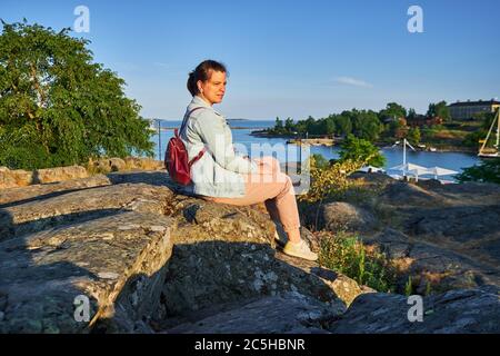 Die Frau sitzt auf dem Stein und blickt auf den Sonnenuntergang im Kaivopuisto Park, Helsinki, Finnland Stockfoto