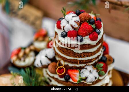 Hochzeitstorte mit Obst und einem alten Holztisch mit Nadeln von Zapfen und Blättern während einer Hochzeitszeremonie im Winter auf Schnee in der Mitte eines Waldes Stockfoto