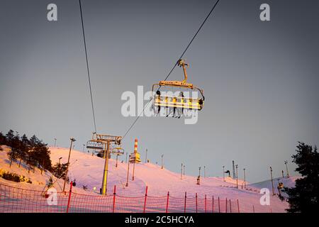 Silhouetten von Skifahrern auf Sesselliften am Abend, Sonnenuntergang Stockfoto