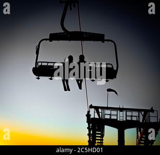 Silhouetten von Skifahrern auf Sesselliften am Abend, Sonnenuntergang gelbes Licht Stockfoto