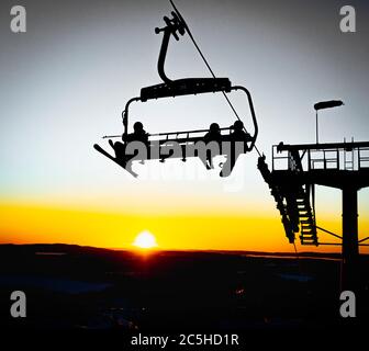 Silhouetten von Skifahrern auf Sesselliften am Abend, Sonnenuntergang gelbes Licht Stockfoto