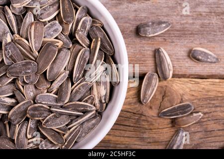 Eine Schüssel mit gerösteten und gesalzenen Sonnenblumenkernen in ihren Schalen., über altem Holzhintergrund Stockfoto