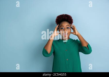 Schockiert, erstaunt. afroamerikanische junge Frau Porträt isoliert auf blauem Studio-Hintergrund. Schönes weibliches Modell. Konzept der menschlichen Emotionen, Gesichtsausdruck, Verkauf, Anzeige. Copyspace. Stockfoto