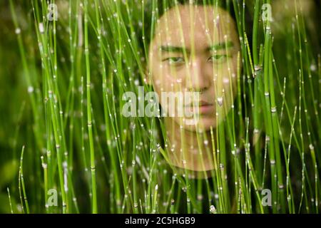 Junger asiatischer Mann mit langen Haaren im Park mit mehrfacher Belichtung Stockfoto
