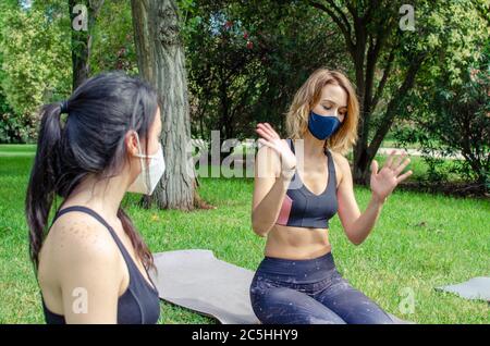 Frau, die einem Freund in einem Park ein Problem erklärt und Gesichtsmasken trägt Stockfoto