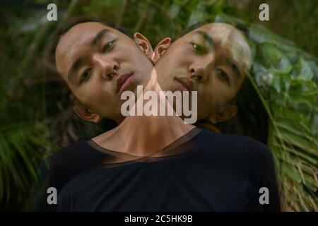 Junger asiatischer Mann mit langen Haaren im Park mit mehrfacher Belichtung Stockfoto
