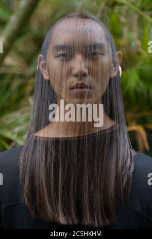 Junger asiatischer Mann mit langen Haaren im Park mit mehrfacher Belichtung Stockfoto