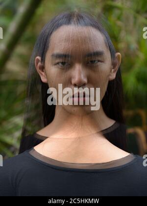 Junger asiatischer Mann mit langen Haaren im Park mit mehrfacher Belichtung Stockfoto