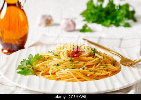 Spaghetti con la colatura di alici, Spaghetti mit Sardellensoße, Pimento-Pfeffer, Knoblauch und Petersilie auf einem weißen Teller mit einer Flasche Fischsoße auf t Stockfoto