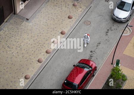 UKRAINE, KIEW - 20. Mai 2020: Der Mann in einem weißen Schutzanzug und einer Maske geht auf einer Straße, um Innenflächen in Gebäuden zu sanieren Stockfoto