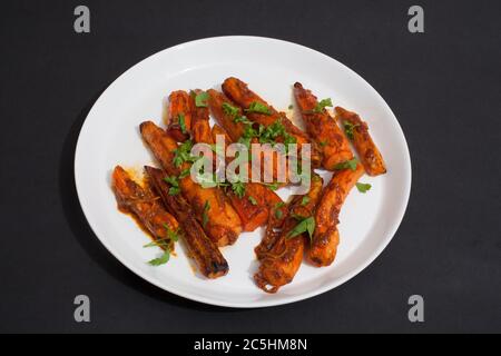 Würzige tunesische Karotten auf einem weißen Teller vor schwarzem Hintergrund Stockfoto