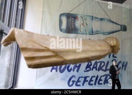 03. Juli 2020, Mecklenburg-Vorpommern, Güstrow: Eine große Werbefahne der Firma Güstrower Schlossquell, mit der Aufschrift "Barlach hätte das auch gefeiert", mit der Illustration einer schwimmenden Flasche hängt hinter der Barlacher Skulptur "das schwimmende" ("Güstrower Ehrenmal"). Im Barlach Museum präsentierte Geschäftsführerin Magdalena Schulz-Ohm die Sonderausstellung "Barlach im Alltag - Alltag mit Barlach". In der Ausstellung von 04.07-27.09.2020 wird neben ausgewählten Werken von Ernst Barlach gezeigt, wie andere Künstler Barlachs Motive aufgreifen und wie Stockfoto