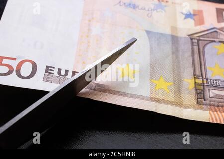 Schere schneiden eine Euro-Rechnung Nahaufnahme auf schwarzem Hintergrund Stockfoto