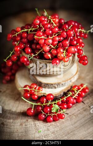 Frische rote Johannisbeeren auf dem Teller auf einem rustikalen Holztisch. Hintergrund mit Kopierbereich. Selektiver Fokus. Vertikal. Stockfoto