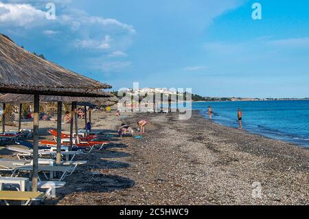 Griechischer Strand an der Ägäis am frühen Morgen. Die Sonne ist gerade aufgegangen und die ersten Schwimmer kommen. Die Liegestühle sind arrangiert und warten Stockfoto