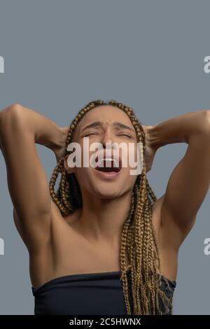 Frustrierte junge Afrikanerin, die ihren Kopf in den Armen hält und vor Schmerzen schreit Stockfoto