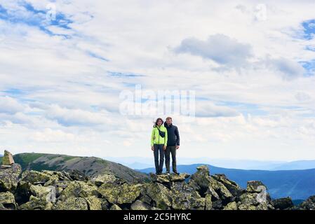 Vorderansicht des liebevollen Paares Umarmung, Posen und Blick auf die Kamera, schöne Berglandschaft im Hintergrund. Bergwandern, Touristen erreichen Gipfel zusammen. Wilde Natur, Sporttourismus Konzept. Stockfoto