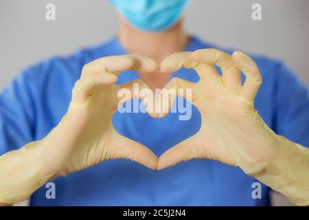 Hände in Gummihandschuhen, die das Herz Symbol vor einem Arzt in Uniform. Stockfoto