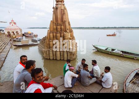 Varanasi, Uttar Pradesh, Indien : EINE Gruppe von Männern sitzt neben dem teilweise versunkenen Ratneshwar Mahadev Tempel auch bekannt als der schiefe Tempel von Varanas Stockfoto