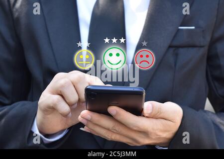 Geschäftsmann drücken Gesicht Emoticon im Smartphone auf dem Display auf dem virtuellen Bildschirm. Konzept der Bewertung der Kundenzufriedenheit und des Feedbacks. Stockfoto