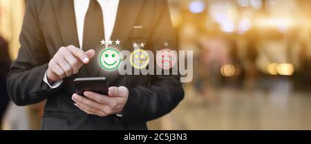 Geschäftsmann drücken Gesicht Emoticon im Smartphone auf dem Display auf dem virtuellen Bildschirm. Konzept der Bewertung der Kundenzufriedenheit und des Feedbacks. Stockfoto