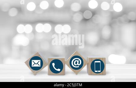 Holzwürfel mit Telefon, E-Mail und Post Icons auf weißem Tisch über verwischen Bokeh hellen Hintergrund. Kontaktieren Sie uns. Stockfoto