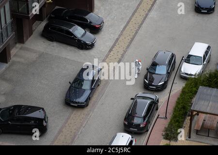 UKRAINE, KIEW - 20. Mai 2020: Der Mann in einem weißen Schutzanzug und einer Maske geht auf einer Straße, um Innenflächen in Gebäuden zu sanieren Stockfoto