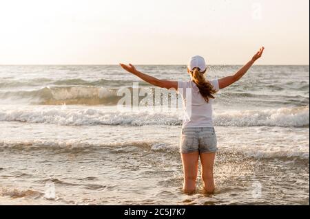 Mädchen in einem weißen T-Shirt und Mütze steht gegen das Meer Stockfoto