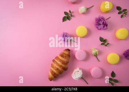 französisches Gebäck - Makronen und Croissant mit Blumen auf rosa Hintergrund mit Kopierraum. Draufsicht Stockfoto