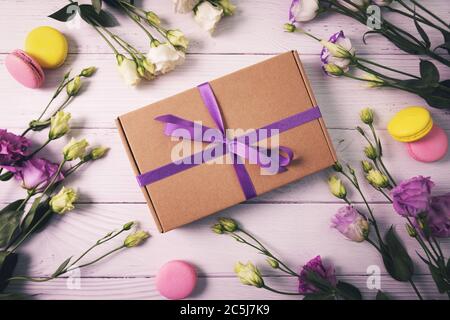 Geschenkbox mit Blumen und Makronen auf weißem Holzhintergrund. Grußkarte zum Geburtstag, Muttertag oder Valentinstag Stockfoto