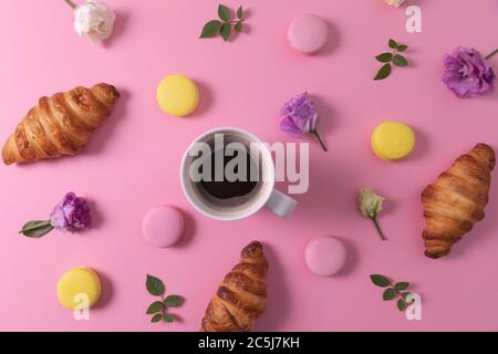 Croissants und Makronen mit Blumen und Tasse Kaffee auf rosa Hintergrund. Draufsicht Stockfoto
