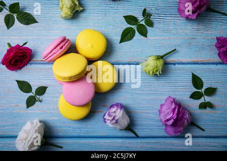 Rosa und gelbe Macarons mit Blumen auf blauem Holztisch. Draufsicht Stockfoto